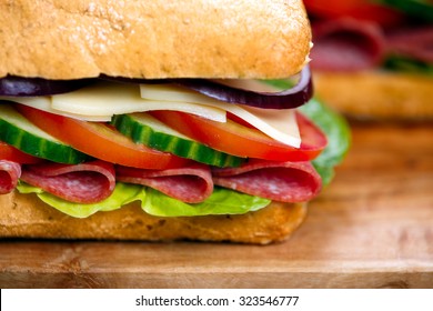 Sandwich with lettuce, slices of fresh tomatoes, cucumber, red onion, salami and cheese.