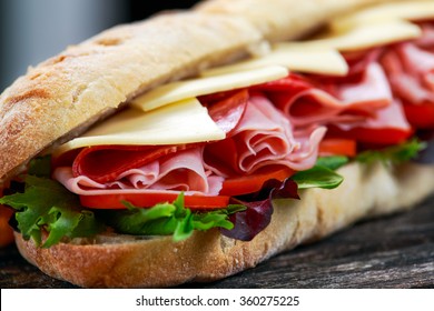Sandwich with lettuce, slices of fresh tomatoes, salami, hum and cheese
