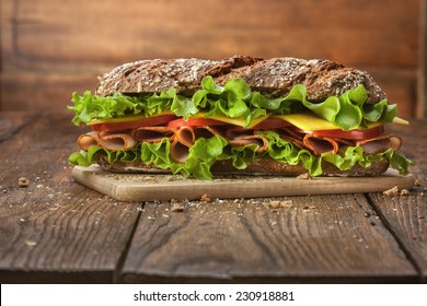 Sandwich on the wooden table with slices of fresh tomatoes, ham, cheese and lettuce - Powered by Shutterstock