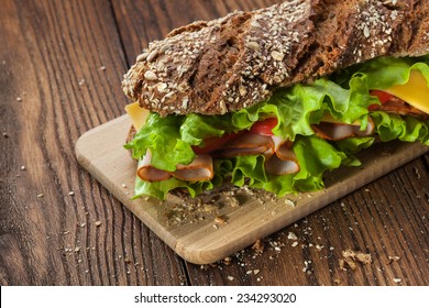 Sandwich on the wooden table with slices of fresh tomatoes, ham, cheese and lettuce - Powered by Shutterstock