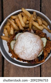 Sandwich. Overhead View Of A Crispy Fried Chicken Sandwich With Bacon, Cucumber And French Fries In A Metal Dish On The Wooden Table.