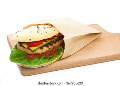 Sandwich In Paper Package With Meat Cutlet On Chopping Board With A Row Lying Tomatoes On A White Background, Nobody. Sandvich With A Stuffing From Meat Cutlet, Vegetables And Mayonnaise With Ketchup.