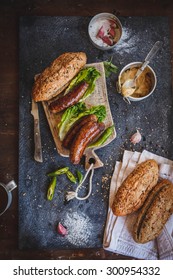 Sandwich Recipe - Bread Roll, Grilled Sausage, Green Salad Leaves, Yellow Mustard And Basil. Ingredients On Black Chalkboard From Above. Poster Layout With Free Text Space.