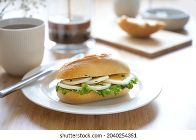 Sandwich Roll With Egg Slices, Lettuce And Chives Garnish On A White Plate And Fresh Coffee On A Light Wooden Breakfast Table, Selected Focus, Narrow Depth Of Field