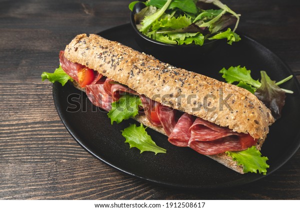 Sandwich with salami tomatoes and lettuce leaves.\
Healthy takeaway lunch