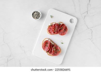 Sandwich, toast with cream cheese, sliced salami, sausage, microgreen on white cutting board. Snack, bruschetta. Top view. Copy space.