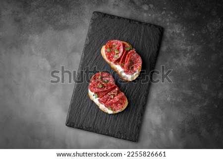 Sandwich, toast with sliced salami, pepperoni, cream cheese, sausage, microgreen on dark slate cutting board. Snack, bruschetta. Top view. Copy space.