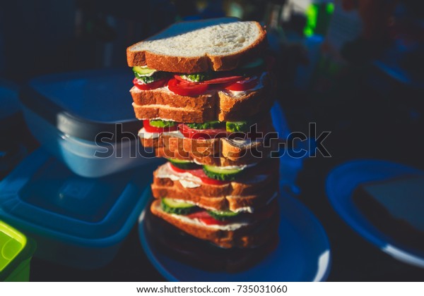 A sandwich tower outdoors, camping sandwiches made
of cheese, ham, toast, cucumber and tomato, road trip breakfast,
travel lunch