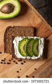 Sandwich With White Minced Curd And Slices Of Avocado On The Homemade Bread. Half Of Avocado And Some Peppers On The Wooden Cutting Board Next To The Sandwich. Top View. Rustic Atmosphere. 