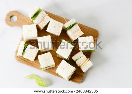 Sandwich of white soft bread with ham, cheese and fresh lettuce, square cut, three layers sandwich bread.