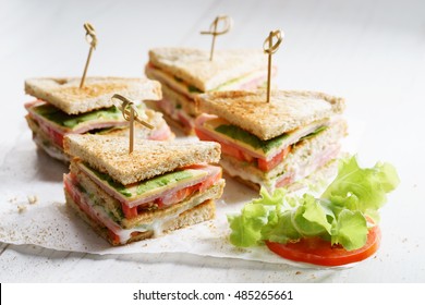 Sandwich of whole wheat bread with ham, cheese and fresh tomato, triangle cut, three layers sandwich bread