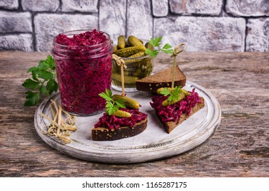 Sandwiches with beet and pickled cucumber on dark bread on a wooden background. Selective focus.