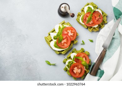 Sandwiches on green wafer with spinach and mozzarella cheese, pesto sauce, tomatoes and basil on a gray concrete old background. Selective focus. Top view. - Shutterstock ID 1022963764