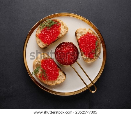 Sandwiches with red caviar and bread in a round plate on a black table, top view