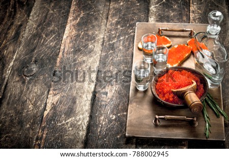 Sandwiches with red caviar and vodka on a tray. On wooden background.
