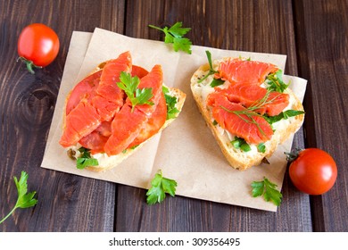 Sandwiches with smoke salmon (trout), cream cheese, tomato and parsley on rustic wooden background close up