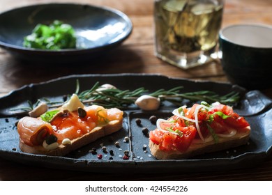 Sandwiches with smoked salmon and tomato on black plate close up. Focus on foreground. Bruschetta with seafood and tomatos, served on wooden background