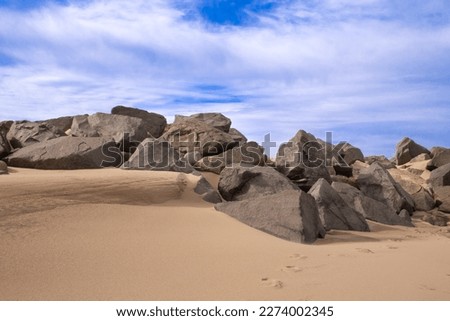Sandy beach with boulders, large rocks. Blue sky with wispy clouds on a winter's day, Sandy Hook Beach, New Jersey, USA, part of Gateway National Recreation Area, known for hiking, camping, birding.