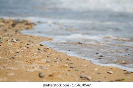 Sandy beach with colorful pebbles and sea foam. The wave is pouring towards the sand.