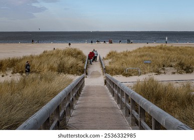 Sandy Beach with Grasses, Wooden Fence, Pathway, and Visitors at the North Sea Coast in Norddeich, Germany - Powered by Shutterstock