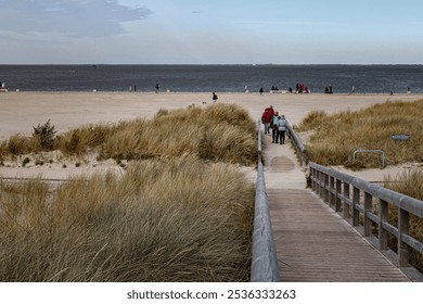 Sandy Beach with Grasses, Wooden Fence, Pathway, and Visitors at the North Sea Coast in Norddeich, Germany - Powered by Shutterstock