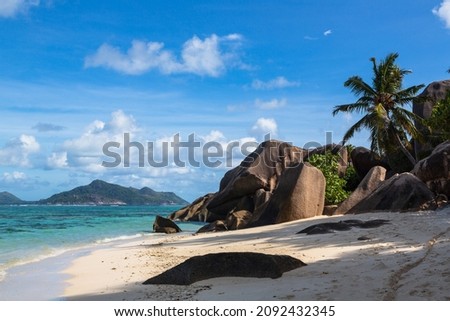 Sandy beach with large granite stones and palm trees, blue IndianOcean and blue sky with clouds. La Digue, the Seychelles