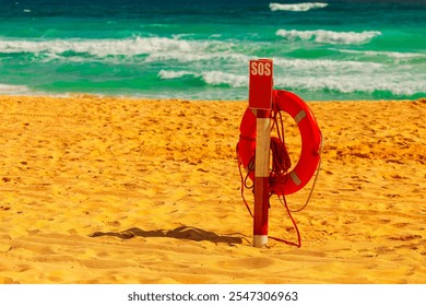 Sandy beach with a lifebuoy attached to wooden post. Inscription SOS provides emergency contact information. Background features the ocean with waves crashing onto shore, indicating a coastal safety  - Powered by Shutterstock