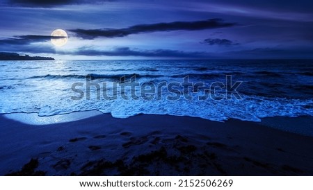 sandy beach at night. beautiful seascape background. calm waves washing the shore. clouds glowing in full moon light. summer vacation and relaxing recreation concept