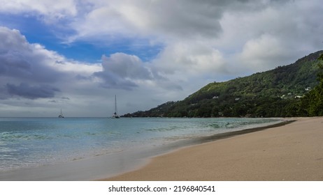 Sandy beach on a tropical island. The turquoise ocean is calm. Yachts are visible in the distance. A green hill against a background of blue sky and clouds. Seychelles. Mahe. Beau Vallon - Shutterstock ID 2196840541