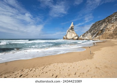Sandy beach with rolling waves and a pointed rock sticking out of the ocean