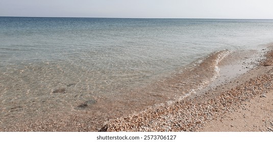 Sandy beach with small seashells, clear water, and gentle waves against the transparent sea. A perfect spot for enjoying nature and relaxation.
