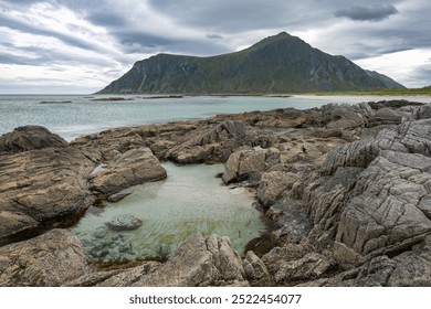 Sandy beach with stones and clear water pond and rocky mountains in cloudy background, Lofoten Norway - Powered by Shutterstock