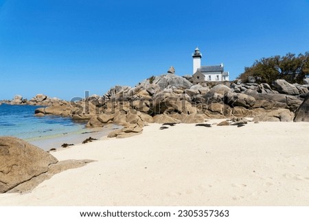 Sandy beach and turquoise waters at the foot of the lighthouse perched on a point surrounded by huge rocks in Finistère - Brittany - France 