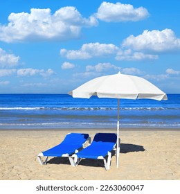 Sandy beach with white sun umbrella and two blue lounges. Magical comfortable warm and clear season of Mediterranean - Powered by Shutterstock