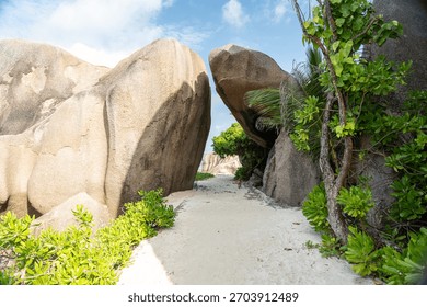 Sandy path between large granite boulders and green plants on Anse Source d Argent beach on La Digue Island Seychelles