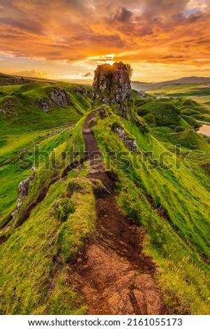 Sandy path to the top of a rock Castle Ewen on the Isle of Skye. Sunset in summer of a landscape in Scotland in the evening with clouds in the sky. Green meadows with hills and a lake