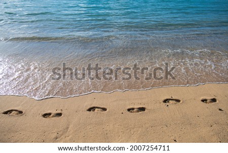 Sandy tropical beach with sea waves. Foot steps on the shore. Footp rints in the sand at sunset.