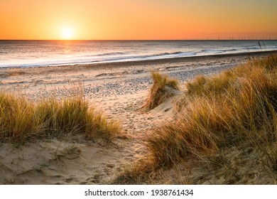 A sandy winding path weaves through the sand dunes and towards the sea on the Norfolk Coast at Winterton on Sea as the early morning sun rises above the horizon. - Powered by Shutterstock