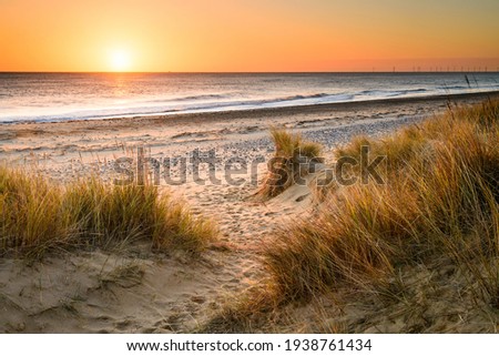 A sandy winding path weaves through the sand dunes and towards the sea on the Norfolk Coast at Winterton on Sea as the early morning sun rises above the horizon.