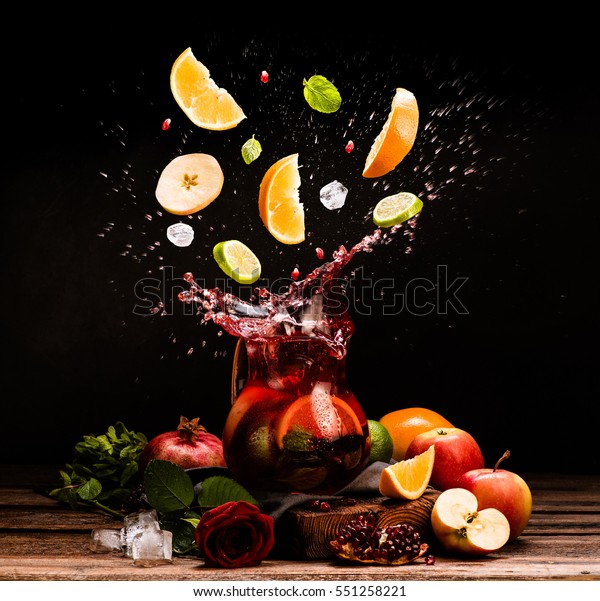 Sangria. Flying fruits. Apple, orange, lime,\
pomegranate, mint. Drink. Wine. Concept. Dark moody. Spain.\
Beverage jug. Juice\
jar.