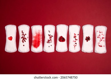 Sanitary napkins with different red items of them on red background. Menstruation cycle period, woman hygiene concept.