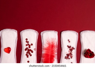 Sanitary napkins with different red items of them on red background. Menstruation cycle period, woman hygiene concept.
