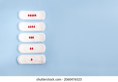 Sanitary Pads Decorated With Cardboard Drops On Blue Background. Concept Intensity Of Menstrual Flow. Place For Text