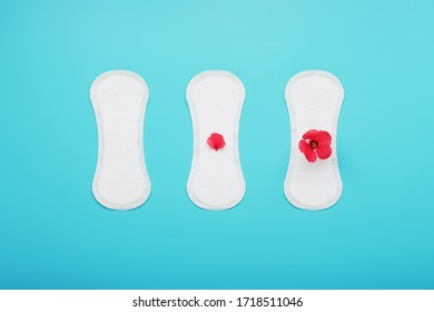 Sanitary Pads In A Row With A Red Flower On A Blue Background. The Concept Of Critical Days, Stages Of The Menstrual Cycle.