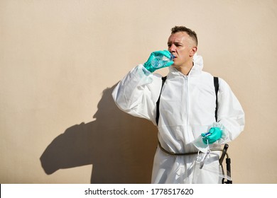 Sanitation Worker In Hazmat Suit Having A Water Break And Refreshing Himself After Disinfecting Due To Coronavirus Pandemic. 