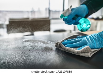 Entschlackende Oberflächen, die den Küchentisch mit einer desinfektiösen Spritzflasche reinigen, mit Handtuch und Handschuhen. COVID-19 Präventivmaßnahmen im Inneren.
