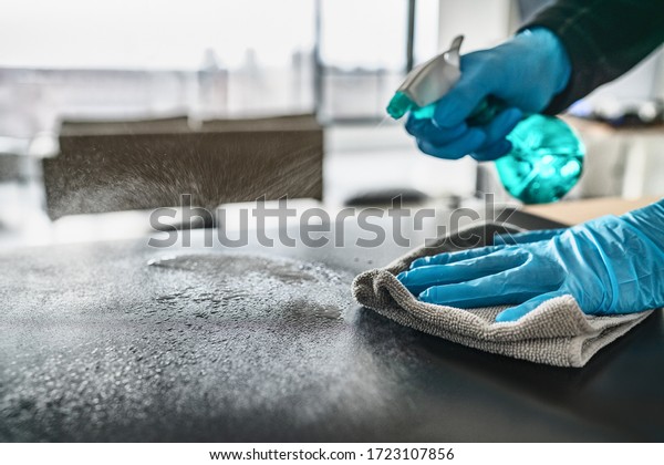 Sanitizing surfaces cleaning home\
kitchen table with disinfectant spray bottle washing surface with\
towel and gloves. COVID-19 prevention sanitizing\
inside.
