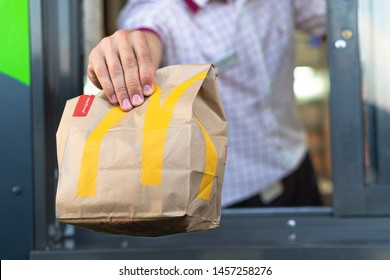 Sankt-Petersburg/Russia - July 21 2019: McDonalds worker holding bag of fast food. Hand with a paper bag through the window of mcdonalds car drive thru service.