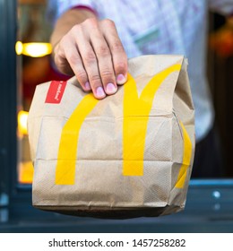 Sankt-Petersburg/Russia - July 21 2019: McDonalds Worker Holding Bag Of Fast Food. Hand With A Paper Bag Through The Window Of Mcdonalds Car Drive Thru Service.