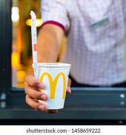 Sankt-Petersburg/Russia - July 21 2019: McDonald's Worker Holding Paper Cup With A Straw. Hand With A Coca Cola Drink Through The Window Of Mcdonalds Car Drive Thru Service.